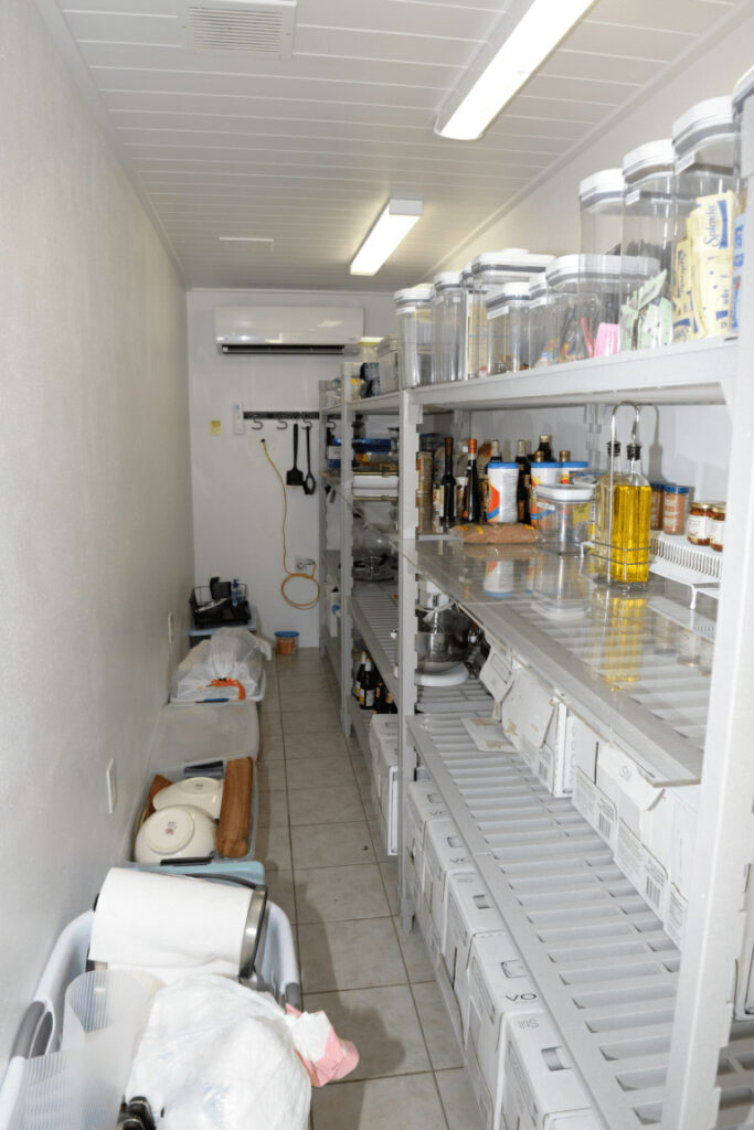 Spesa di ottobre: fare il giro della dispensa prima di uscire EFTA00001876 - Well-organized kitchen pantry with shelves stocked with food items and supplies including jars of condiments and cleaning products